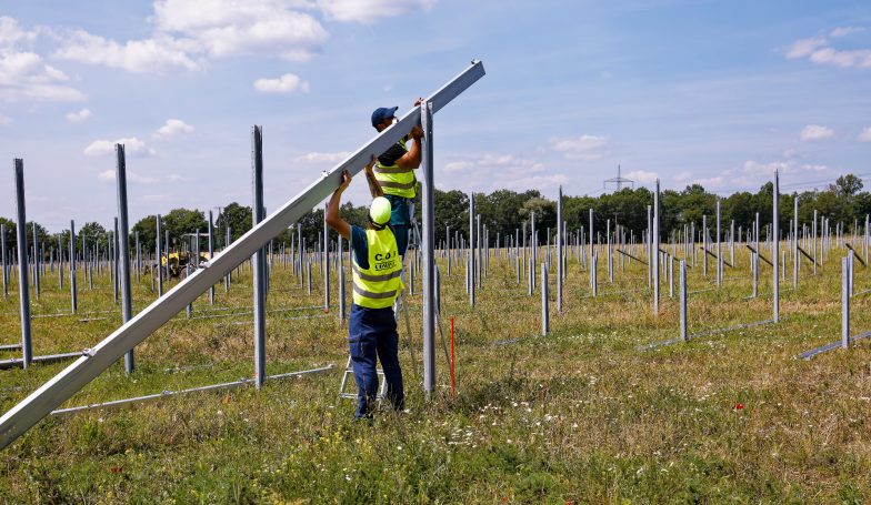 Zwei Bauarbeiter, die auf einer Wiese Unterkonstruktionen von Solar-Paneelen montieren. 